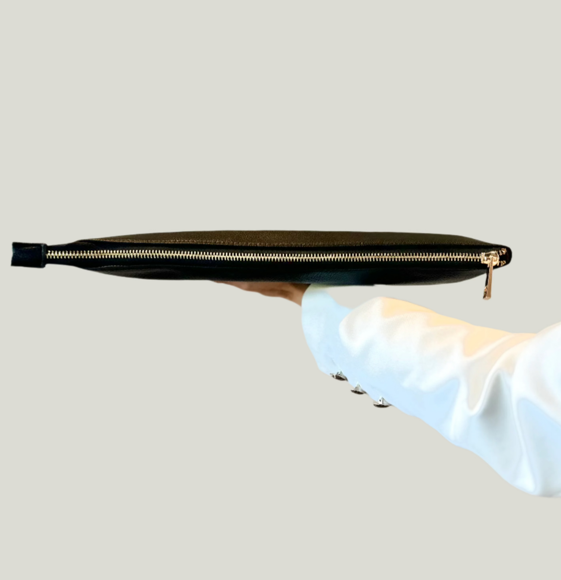 Black clutch bag with gold zipper held by a hand on a light gray background